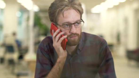 Bearded Smiling Guy with Glasses and Casual Plaid Shirt Talking on a Cell Phone.