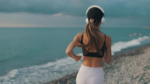 A Young Woman Runner is Listening to Music in Earphones and Training By a Sea