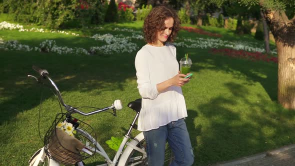 Portrait of a Young Woman Surfing in the Internet Using Her Smartphone Standing in the City Park