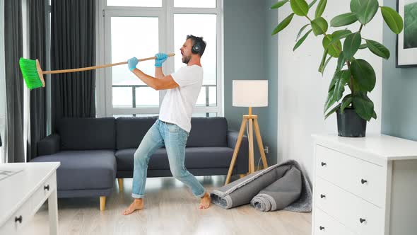 Man in Headphones Cleaning the House Fooling Around and Having Fun Dancing and Singing with a Broom