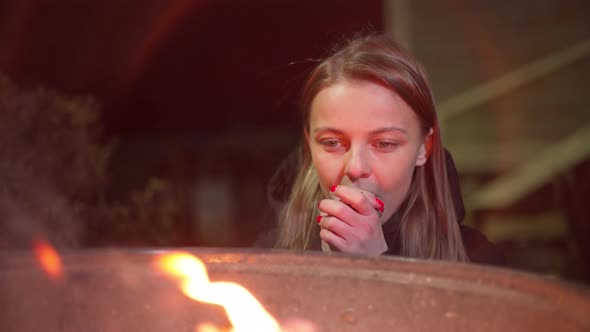 A Caucasian Girl Warms Up Near the Fire