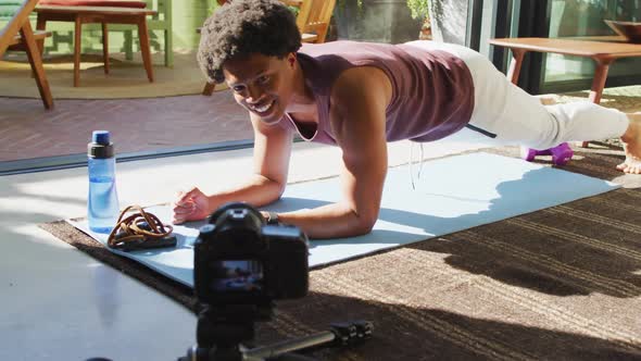 Smiling fit african american man exercising at home, doing press ups and filming fitness vlog