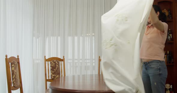 a Woman in a Pink Tshirt and Blue Jeans Puts on a White Tablecloth