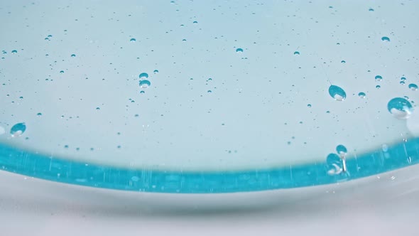 Transparent Blue Cosmetic Gel Fluid with Bubbles Flowing Down on a White Surface