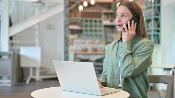 Woman with Laptop Talking on Smartphone in Cafe