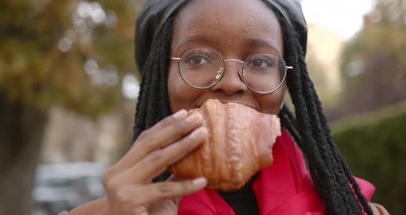 Young Black Girl with a Croissant in Her Hands in the Middle of the Street