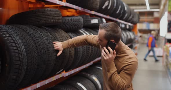 Man Chooses Winter Car Tires in Auto Shop Consulting By Smartphone