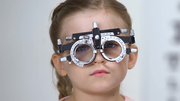 Male Ophthalmologist Choosing Eyeglasses Lens for Small Girl Wearing Phoropter