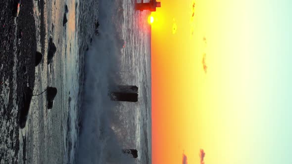 waves crash against old reinforced concrete pillars on the beach at sunset