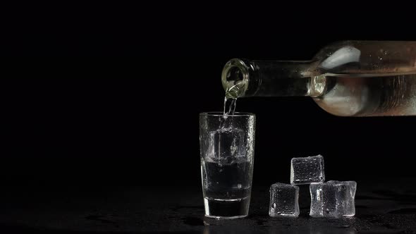 Bartender Pouring Up Shot of Vodka with Ice Cubes From Bottle Into Shot Glass on Black Background