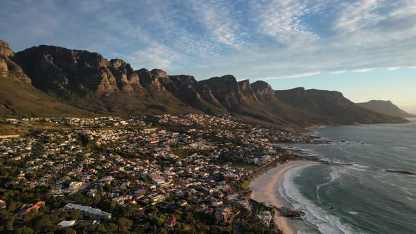 Camps Bay beach coastline at sunset with twelve apostles in background, aerial