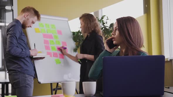 Businesswoman with Laptop Computer Calling on Smartphone at Office