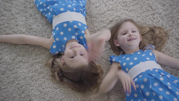 Top View of Cute Little Caucasian Girls Waving at Camera and Smiling. Joyful Brunette Twin Sisters