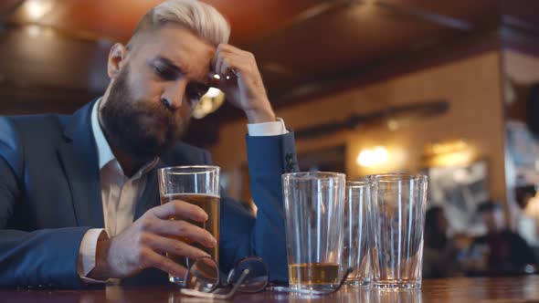 Young Businessman Sitting at Bar Counter with Beer Glass in Hand While Resting After Hard Working