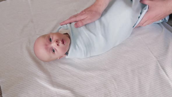 Father Swaddles a Newborn Son in a Blue Diaper