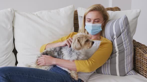 Woman wearing face mask holding her pet dog at home