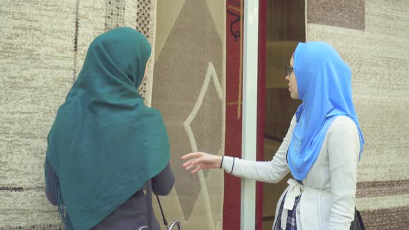 Two Young Muslim Women in Hijabs Choose Carpet