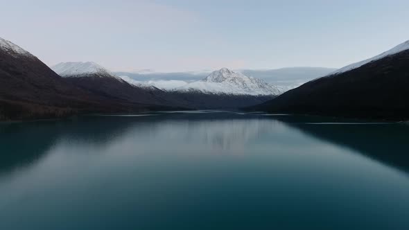 Drone shoots a frozen lake among snow-capped mountains in the evening in Eklutna Lake, Alaska, USA