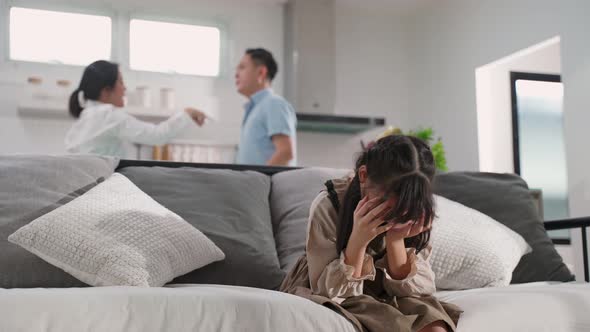 Asian girl kid sitting and crying on bed while parents having fighting or quarrel conflict at home.