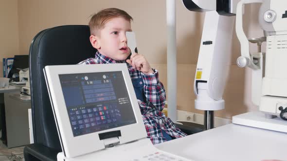 Ophthalmologist Treatment in the Clinic - a Little Boy Covers His Eye with an Eye Shield and Read