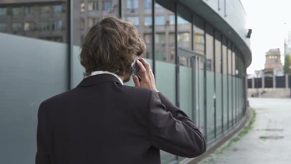 A businessman is talking on the phone on his way to work in a big city.