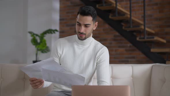 Stressed Young Man Throwing Away Papers Holding Head in Hands Sitting in Home Office Indoors