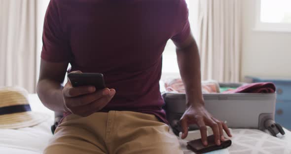 Midsection of biracial man preparing for travel, showing smartphone with covid-19 passport on screen