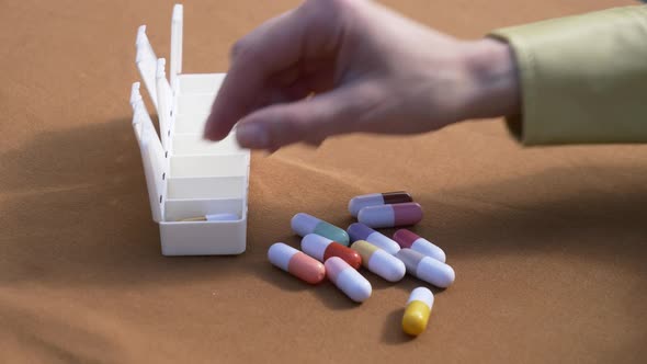 Female hand sorting pills in pillbox on brown background