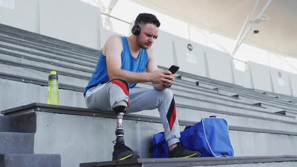 Caucasian disabled male athlete with prosthetic leg sitting, wearing headphones