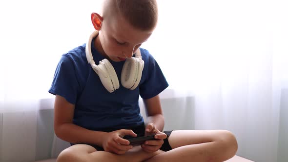 Child's dependence on a mobile device theme. Child with headphones on neck is sitting on table