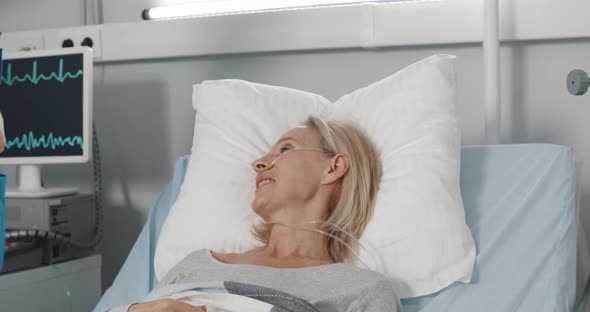 Woman Doctor in Safety Mask Talking and Examining Health of Senior Patient in Hospital Ward