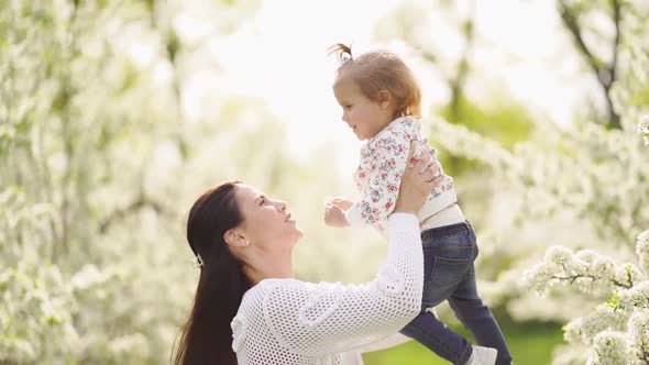 Mom Throws Up Her Daughter in the Park By a Flowering Tree