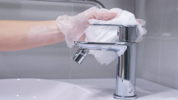 Woman's Gloved Hand Cleans a Stainless Steel Water Tap in the Bathroom with Detergent. Hygiene in