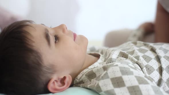 A Beautiful Girl Kisses a Small Child with Short Hair While He is Sleeping