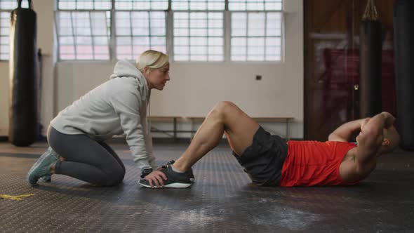 Caucasian muscular man exercising, doing sit ups with female coach