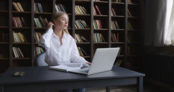 Business Woman in a White Shirt Works at a Laptop and Takes Notes