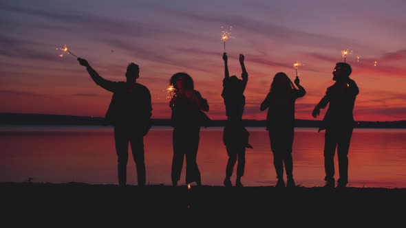 Friends with Burning Sparklers Dancing at Night Enjoying Outdoor Party on Beach