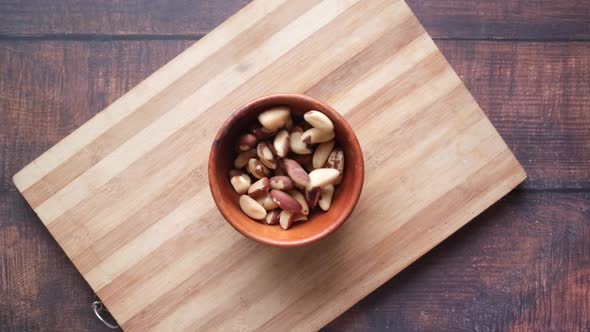 Top View of Brazilian Nut Dropping in a Bowl on Wooden Background