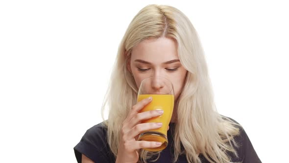 Young Cute Smiling Blonde Girl Wearing Dark Blue Shirt Drinking Orange Juice From Glass on White