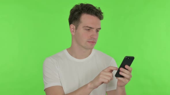 Young Man Browsing Smartphone on Green Background