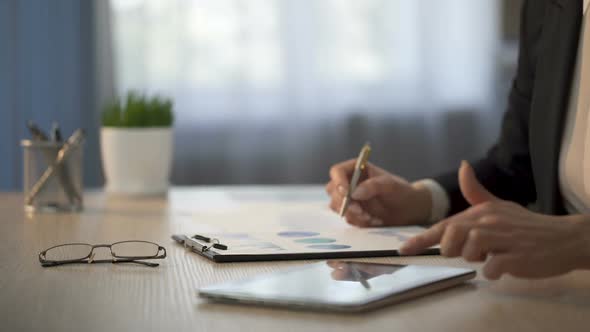 Female Employee Looking for Information on Tablet, Marking Printout Graphs, Data