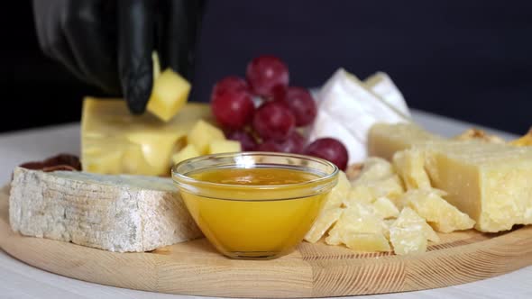 Preparation of cheese plate with hard cheeses camembert, brie, parmesan, dutch cheese, grapes, honey