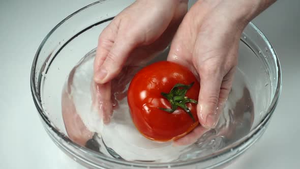Slow Motion, Female Hands Wash Ripe Red Tomato in Clean Water. Fresh Juicy Tomato with Green Stem in