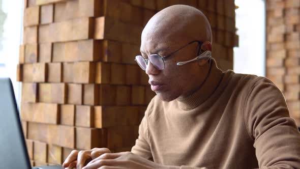 An African American Man with a Serious Expression Works with a Laptop and Documents at Home