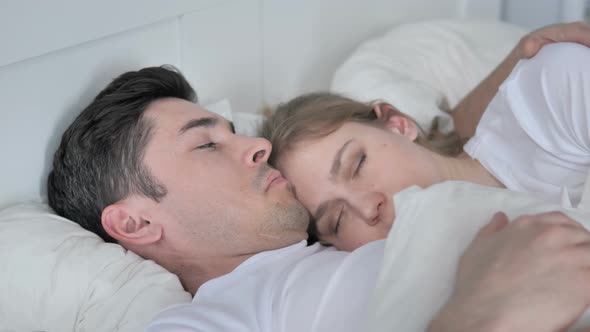 Thinking Pensive Man Lying in Bed and Cuddling Sleeping Girlfriend