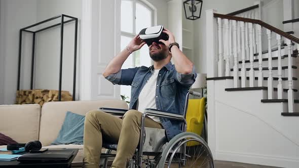 Bearded Man in Wheelchair Enjoying Watching Futuristic Video Using Virtual Reality Headset at Home
