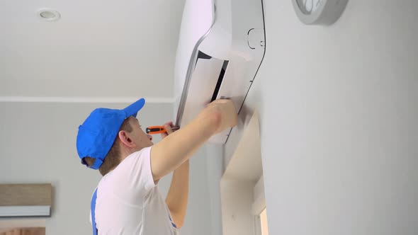 A young master in uniform repairs the air conditioner in the apartment.