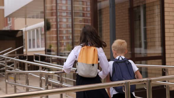 Small Children with Backpacks Run Through the School Yard to the Entrance