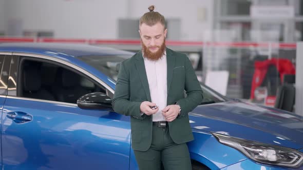 Portrait of Handsome Bearded Caucasian Man Posing in Car Dealership with Keys From New Automobile