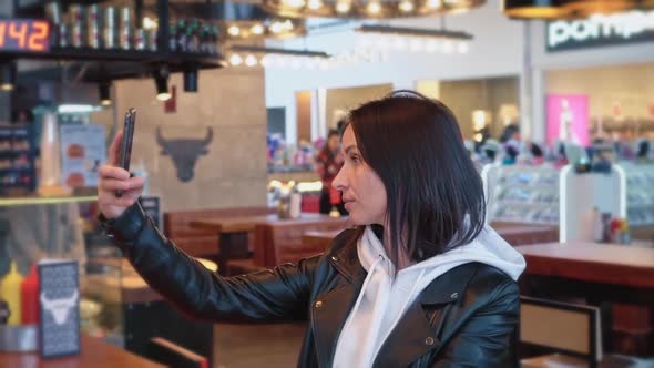 A Brunette Woman of Caucasian Nationality in a White Sweater and Black Jacket Sits in a Cozy Cafe